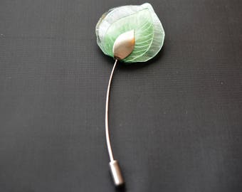 May include: A green glass flower brooch with a silver leaf detail. The brooch is attached to a silver pin.