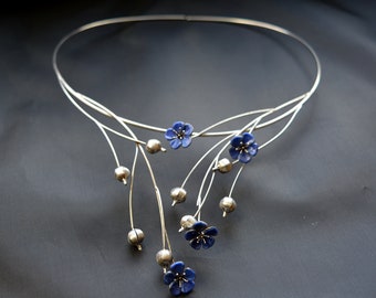 May include: A silver necklace with a delicate design featuring blue flower accents. The necklace has a curved shape and multiple branches with small silver beads.