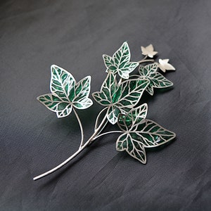 May include: A silver and green ivy leaf brooch with a delicate design. The leaves are cut out and have a green enamel finish.