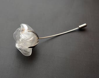 May include: A clear plastic flower brooch with a silver stem and pin. The flower has a delicate, layered design.