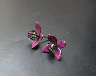 May include: A pair of handcrafted floral stud earrings. Each earring features a magenta flower with green accents in the center. The earrings are set against a dark background.