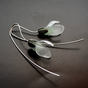 May include: A pair of silver earrings with delicate white flower charms. The flowers have a translucent, almost glass-like appearance.