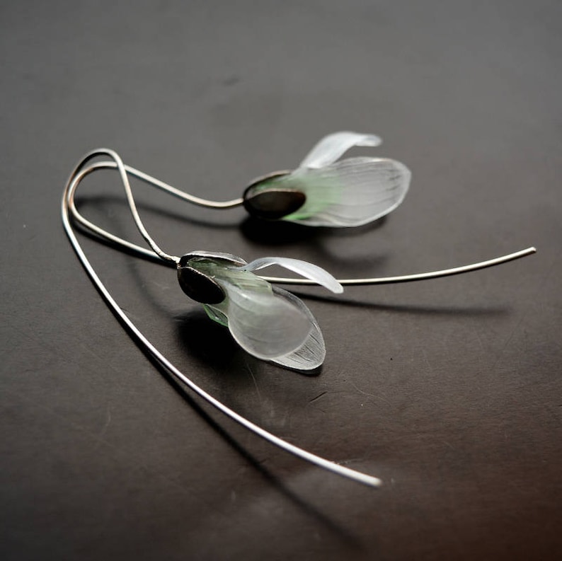 May include: A pair of silver earrings with delicate white flower charms. The flowers have a translucent, almost glass-like appearance.