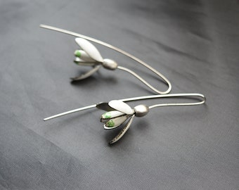 Puede incluir: Un par de pendientes de plata con abalorios de flores blancas y detalles verdes. Las flores tienen un diseño delicado y detallado.