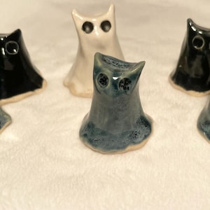 以下が含まれることがあります： さまざまな色のセラミック製のフクロウの置物のコレクション。フクロウは青、黒、白の色合いで、目の詳細な特徴があります。置物は光沢のある仕上げで、白い表面に配置されています。