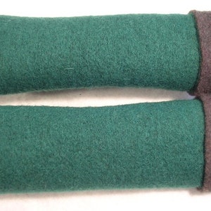 Könnte beinhalten: Zwei grüne Filz-Armwärmer mit braunem Fleece-Futter. Die Armwärmer sind aufgerollt und haben eine weiche, flauschige Textur.