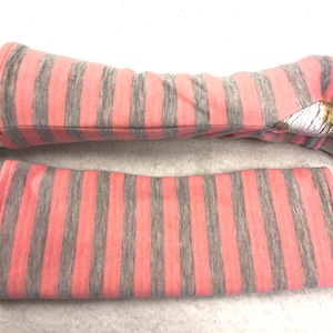 Puede incluir: Un par de calentadores de brazos de rayas rosas y grises. Los calentadores de brazos están hechos de una tela suave y elástica, perfectos para mantener tus brazos calientes en los meses más fríos.