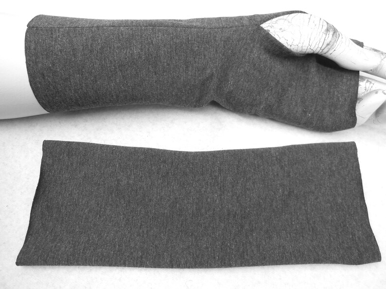 Op de afbeelding: Een paar grijze vingerloze armwarmers, een gevouwen en een uitgevouwen. De armwarmers zijn gemaakt van een zachte, rekbare stof.
