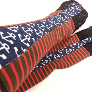 May include: A pair of red and brown striped leg warmers with a navy blue anchor print. The leg warmers have a black lace trim.