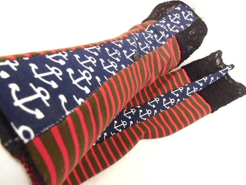 May include: A pair of red and brown striped leg warmers with a navy blue anchor print. The leg warmers have a black lace trim.