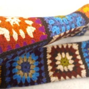 Könnte beinhalten: Ein Paar bunte gehäkelte Armwärmer mit Patchwork-Design, das Quadrate in Orange, Rot, Blau, Grün, Braun und Weiß zeigt.
