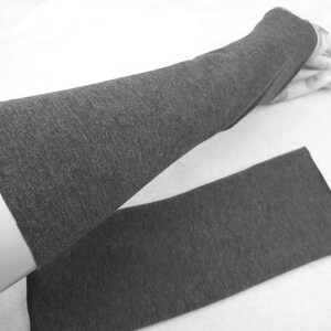 Op de afbeelding: Een paar grijze armwarmers van een zachte, rekbare stof. De armwarmers zijn dubbelgevouwen, met de ene armwarmer bovenop de andere.