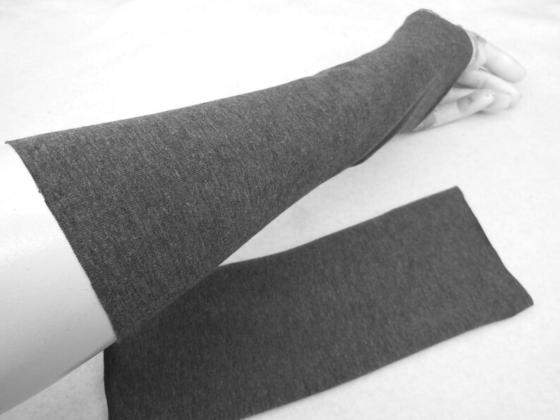 Op de afbeelding: Een paar grijze armwarmers van een zachte, rekbare stof. De armwarmers zijn dubbelgevouwen, met de ene armwarmer bovenop de andere.