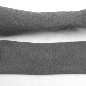 Op de afbeelding: Een grijze stoffen armwarmer, gevouwen en plat gelegd op een wit oppervlak.