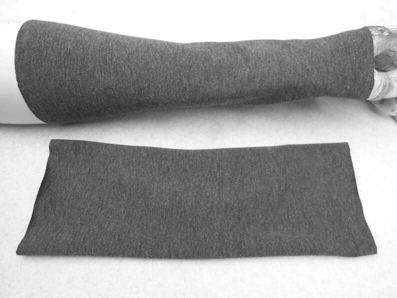 Op de afbeelding: Een grijze stoffen armwarmer, gevouwen en plat gelegd op een wit oppervlak.