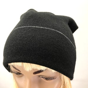 May include: Black beanie with a thin white stripe across the front. The beanie is made of a soft, knit fabric.