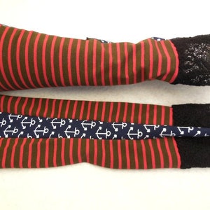 May include: A pair of brown and red striped arm warmers with black lace trim. One warmer has a navy blue band with white anchor print.