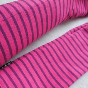 May include: A pair of pink and purple striped arm warmers. The arm warmers are made of a soft fabric and feature evenly spaced stripes. The brand name "WAR ZOO" is visible on a small black tag.