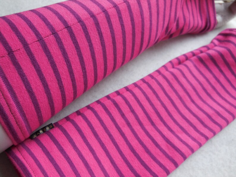 May include: A pair of pink and purple striped arm warmers. The arm warmers are made of a soft fabric and feature evenly spaced stripes. The brand name "WAR ZOO" is visible on a small black tag.