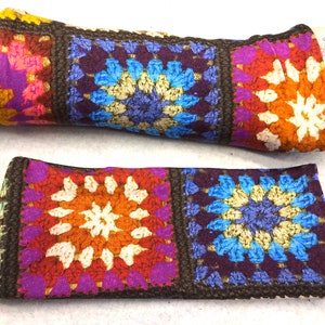 Könnte beinhalten: Ein Paar bunte Häkel-Armwärmer mit braunem Rand. Die Armwärmer haben ein sich wiederholendes Muster aus Quadraten mit einem floralen Design in Orange-, Blau-, Lila- und Weißtönen.