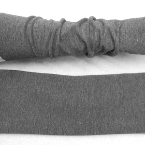 Op de afbeelding: Een paar grijze armwarmers gemaakt van een zachte, rekbare stof. De armwarmers liggen plat op een wit oppervlak.