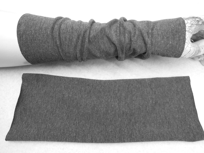 Op de afbeelding: Een paar grijze armwarmers gemaakt van een zachte, rekbare stof. De armwarmers liggen plat op een wit oppervlak.