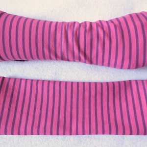 May include: A pair of pink and purple striped arm warmers. One arm warmer is shown on a mannequin arm, while the other is laid flat. The arm warmers are made of a soft, stretchy fabric and feature vertical stripes.