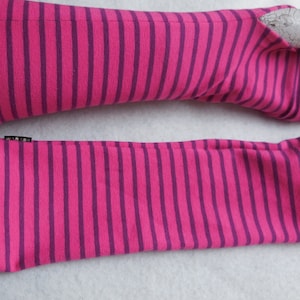 May include: A pair of pink and purple striped fingerless gloves. The gloves are made of a soft material and feature a ribbed cuff. The brand name "WARGO" is on a small black tag. The gloves are designed to cover the hand and forearm.