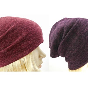 May include: Two slouchy knit beanies in burgundy and dark purple. The beanies are made of a soft, stretchy fabric and have a simple, classic design.