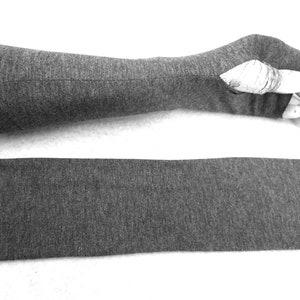 Puede incluir: Un par de guantes sin dedos grises con una larga muñequera. Los guantes están hechos de un tejido suave y elástico. Los guantes están colocados planos sobre una superficie blanca.