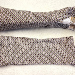 May include: A pair of brown and white patterned fabric arm warmers. The arm warmers are made of a soft, stretchy fabric and have a geometric pattern. The arm warmers are shown on a white surface.