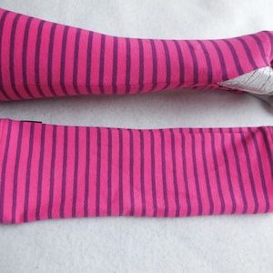 May include: A pair of pink and purple striped arm warmers. One arm warmer is on a mannequin arm, and the other is lying flat. The arm warmers are made of a soft, stretchy fabric and have a thumb hole.
