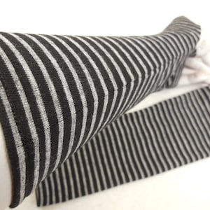 Puede incluir: Un par de calentadores de brazos a rayas negras y grises. Los calentadores de brazos están hechos de una tela suave y elástica, perfectos para mantener tus brazos calientes en los meses más fríos.