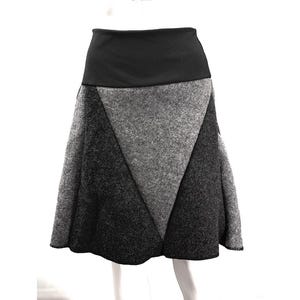 Könnte beinhalten: Ein knielanger Rock mit einem breiten schwarzen Bund und einem Color-Block-Design. Der Rock besteht aus Bahnen aus gefilztem Stoff in Hellgrau, Mittelgrau und Dunkelanthrazit, die in einem geometrischen Dreiecksmuster angeordnet sind.
