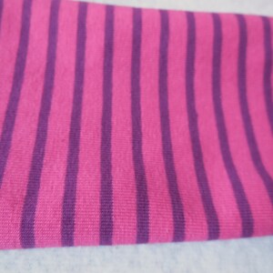 May include: Close-up of a fabric with vertical stripes. The stripes alternate between a bright pink and a deep purple color. The fabric appears to be soft and possibly knitted.