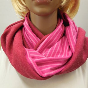 Può includere: Una sciarpa infinita a righe rosa e rosse realizzata in tessuto morbido.