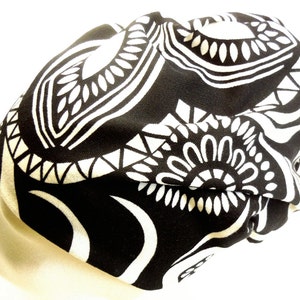 Può includere: Berretto nero e bianco con motivo geometrico. Il berretto è realizzato in un tessuto morbido ed elastico.