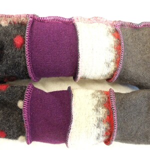 Op de afbeelding: Twee paar handgemaakte vingerloze handschoenen met een patchwork-ontwerp. De handschoenen zijn gemaakt van verschillende stoffen, waaronder wol, vilt en fleece. De handschoenen zijn aan elkaar gestikt met een roze zigzagsteek.