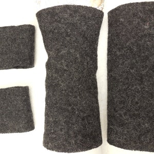 May include: Four pieces of dark charcoal gray felted wool fabric. Two pieces are small rectangles, while the other two are larger, elongated cylindrical tubes. The material has a dense, fuzzy, and fibrous texture throughout all four items.