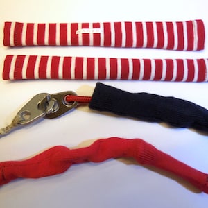 Può includere: Due tubi in tessuto a strisce rosse e bianche, un tubo in tessuto nero, un tubo in tessuto rosso e una clip in metallo argentato con una corda attaccata.