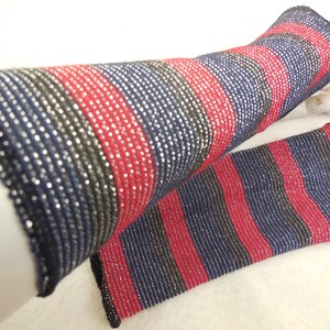 May include: A pair of striped arm warmers in navy blue, black, and red with silver glitter thread. The arm warmers are made of a soft, stretchy fabric.
