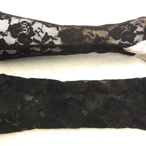 Può includere: Un paio di guanti senza dita in pizzo nero. I guanti sono realizzati in un delicato tessuto di pizzo floreale. I guanti sono mostrati su una mano di manichino e distesi.