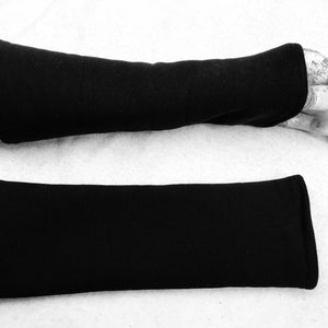以下が含まれることがあります： 黒いフリースの腕カバー2つ。1つの腕カバーは白い表面に平らに置かれています。もう1つの腕カバーはマネキンの腕にあります。