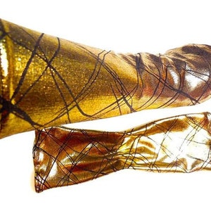 Puede incluir: Un par de calentadores de brazo metálicos dorados con un patrón de cruz negra.