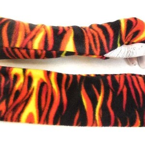 Puede incluir: Un par de calentadores de brazo de vellón negro, rojo y amarillo con un patrón de llama. Los calentadores de brazo se muestran colocados sobre una superficie blanca.
