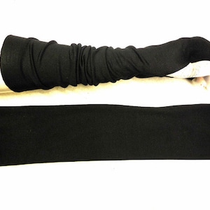 Puede incluir: Un par de guantes negros sin dedos con una larga muñequera. Los guantes están hechos de un tejido suave y elástico y se muestran planos.