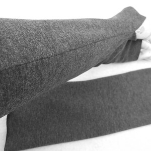 Op de afbeelding: Een paar grijze vingerloze armwarmers gemaakt van een zachte, rekbare stof. De armwarmers zijn gevouwen in de helft, met de naad zichtbaar.