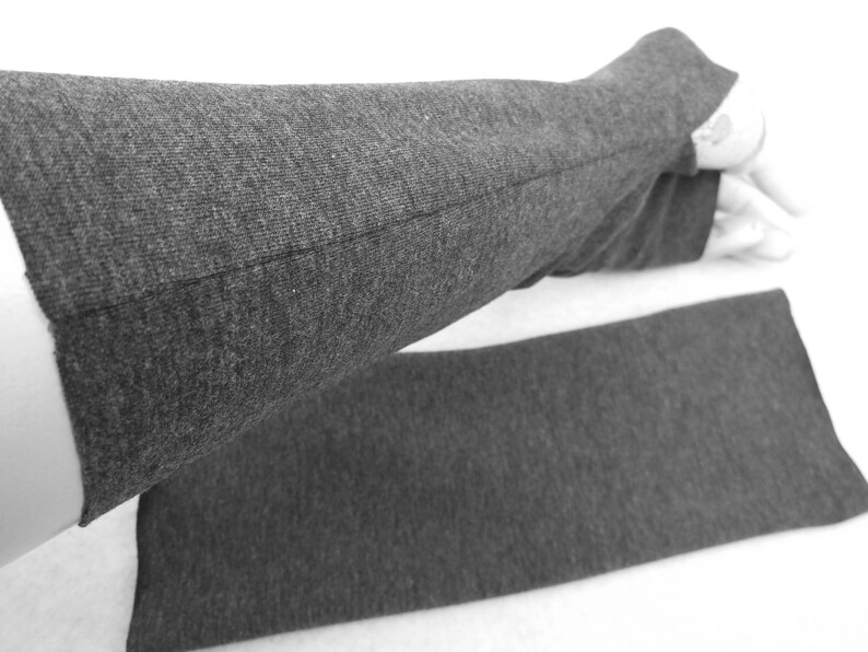 Op de afbeelding: Een paar grijze vingerloze armwarmers gemaakt van een zachte, rekbare stof. De armwarmers zijn gevouwen in de helft, met de naad zichtbaar.