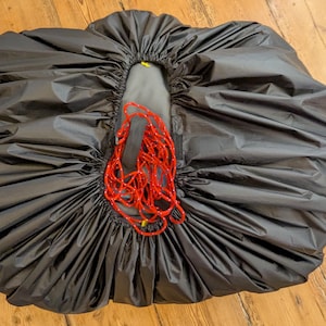 Op de afbeelding: Een zwarte trekkoordtas met een rood koord dat dicht is getrokken. De tas is gemaakt van waterdicht materiaal en is ontworpen om items te beschermen tegen de elementen.