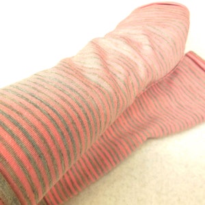 Puede incluir: Un par de calentadores de piernas de rayas rosas y grises. Los calentadores de piernas están hechos de una tela suave y elástica y tienen una textura acanalada.